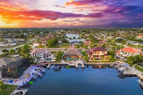 Aerial view of waterfront houses with private docks along a canal under a vibrant sunset sky.