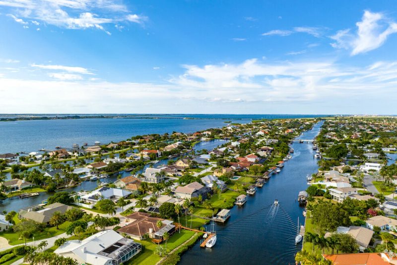 Aerial view of waterfront homes along canals leading to a large body of water under a blue sky.